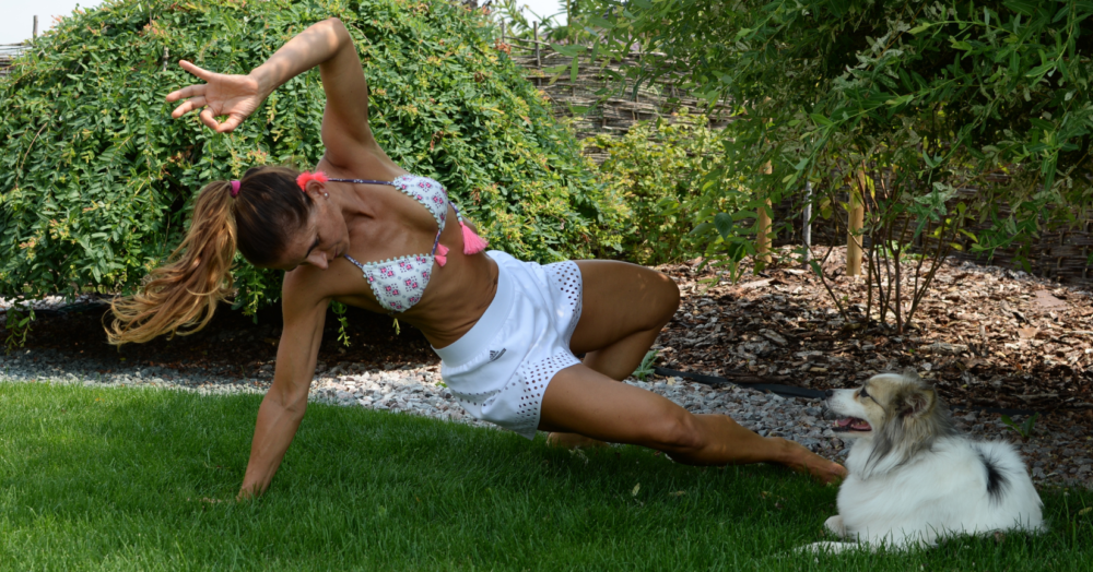 Woman practicing yoga outdoors on green grass with a small dog watching, symbolizing mind-body connection and conscious healing.