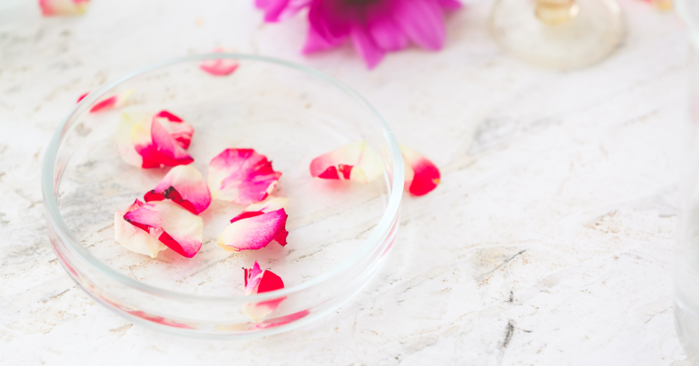 Glass petri dish with pink and white rose petals on a white marble surface, symbolizing natural health and functional medicine.
